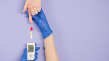Gloved hand testing blood glucose level with meter and blood drop.