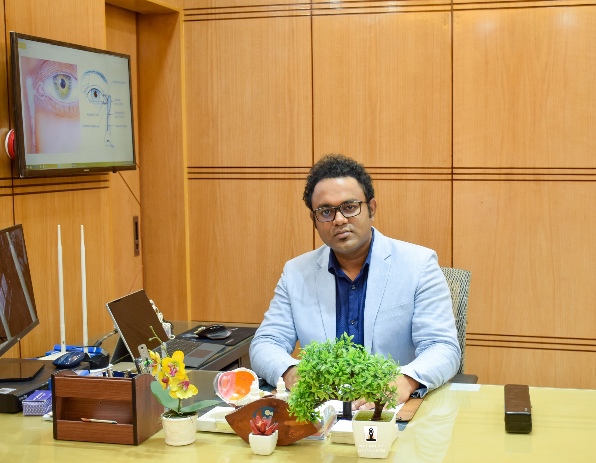Dr. Partha S. Barai, eye specialist and surgeon, sitting at his consultation desk with anatomical eye visuals on the screen.